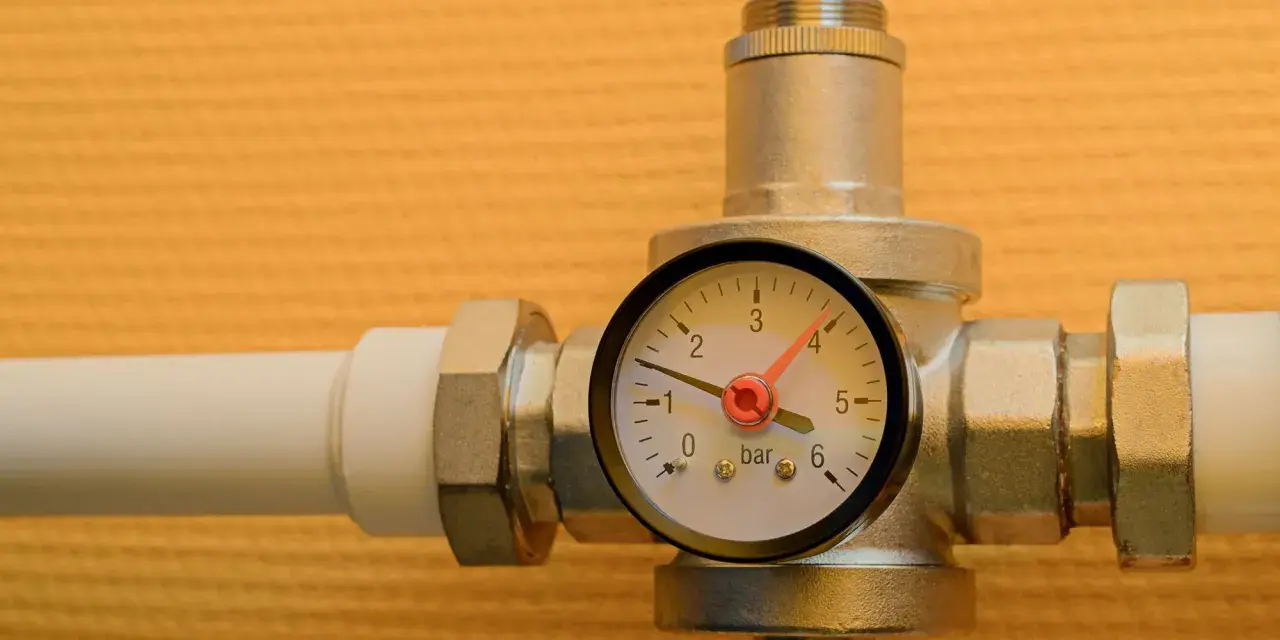 Un réducteur de pression d'eau avec un manomètre indiquant 1 bar. L'appareil est monté sur un tuyau blanc.