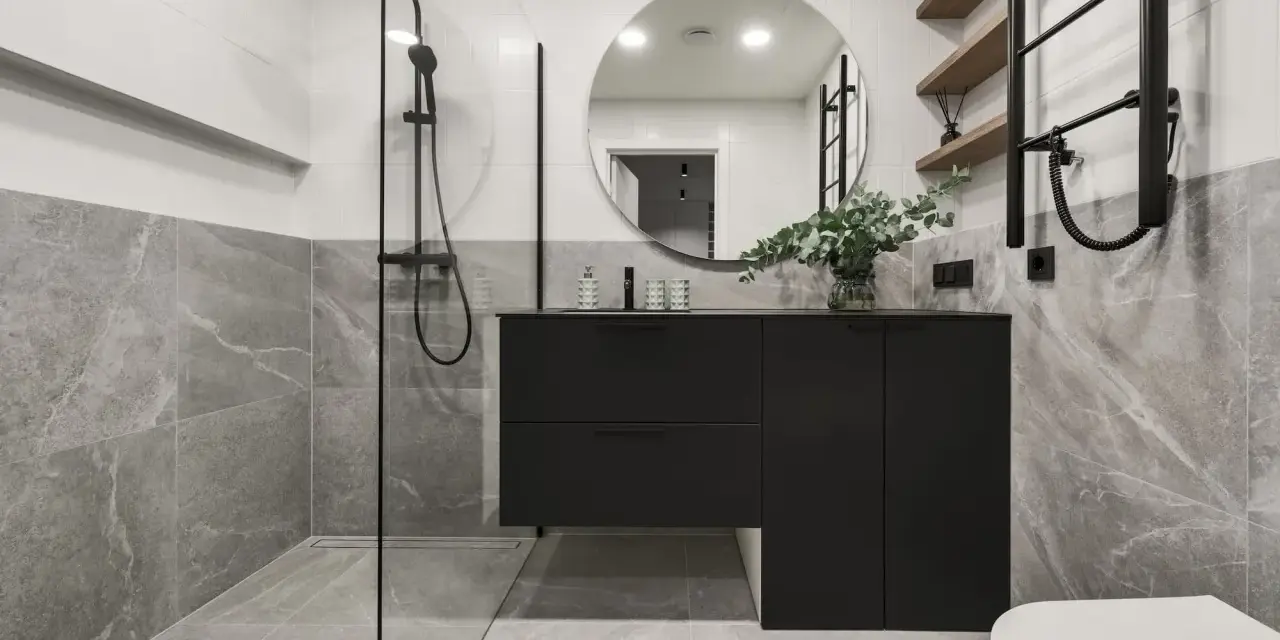 Salle de bain moderne avec douche à l'italienne, meuble suspendu noir, miroir rond et carrelage effet marbre. La construction de cette salle de bain est soignée.