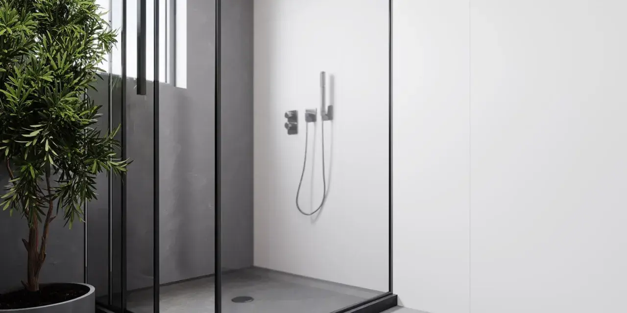 Douche surélevée pour évacuation, avec une paroi en verre et un robinet moderne. Un arbre vert apporte une touche de nature.
