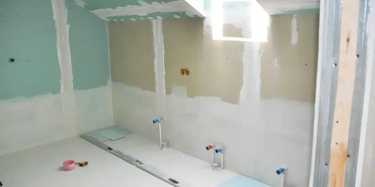 Chantier de salle de bain : murs en plaques de plâtre, tuyauterie apparente, niveau à bulle et outils au sol. Travaux d'isolation salle de bain en cours.
