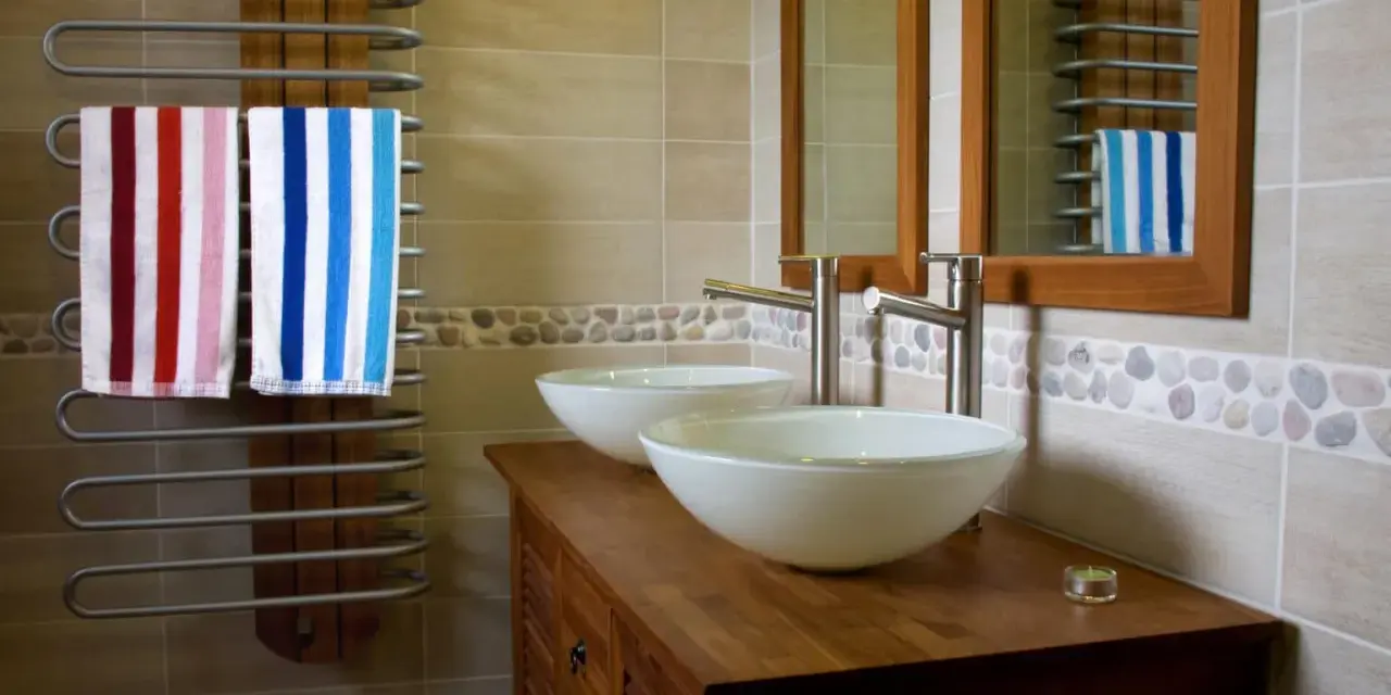 Salle de bain moderne avec double vasque. L'arrivée d'eau est discrète, deux lavabos blancs reposent sur un meuble en bois. Deux serviettes rayées sèchent sur un radiateur.