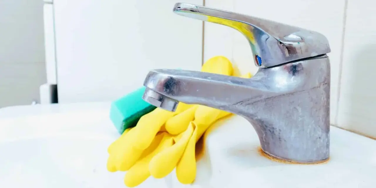 Gants jaunes et éponge verte prêts pour nettoyer robinetterie entartrée.