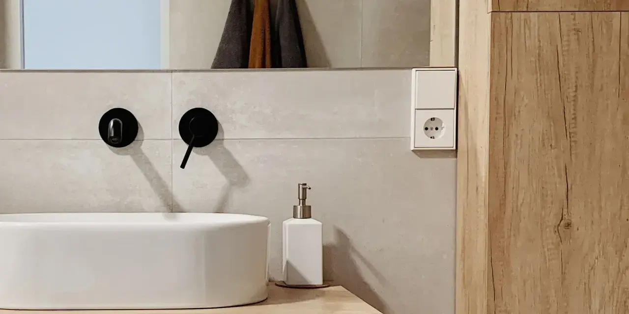 Évier moderne avec robinetterie noire, distributeur de savon et prise électrique. Un détail de la sécurité de la salle de bain.