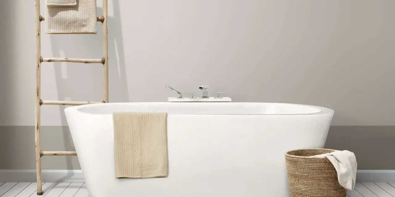 Baignoire moderne avec robinetterie chromée. Un porte-serviettes en bois et un panier en osier complètent l'ensemble, suggérant un émail baignoire poreux à l'aspect naturel.