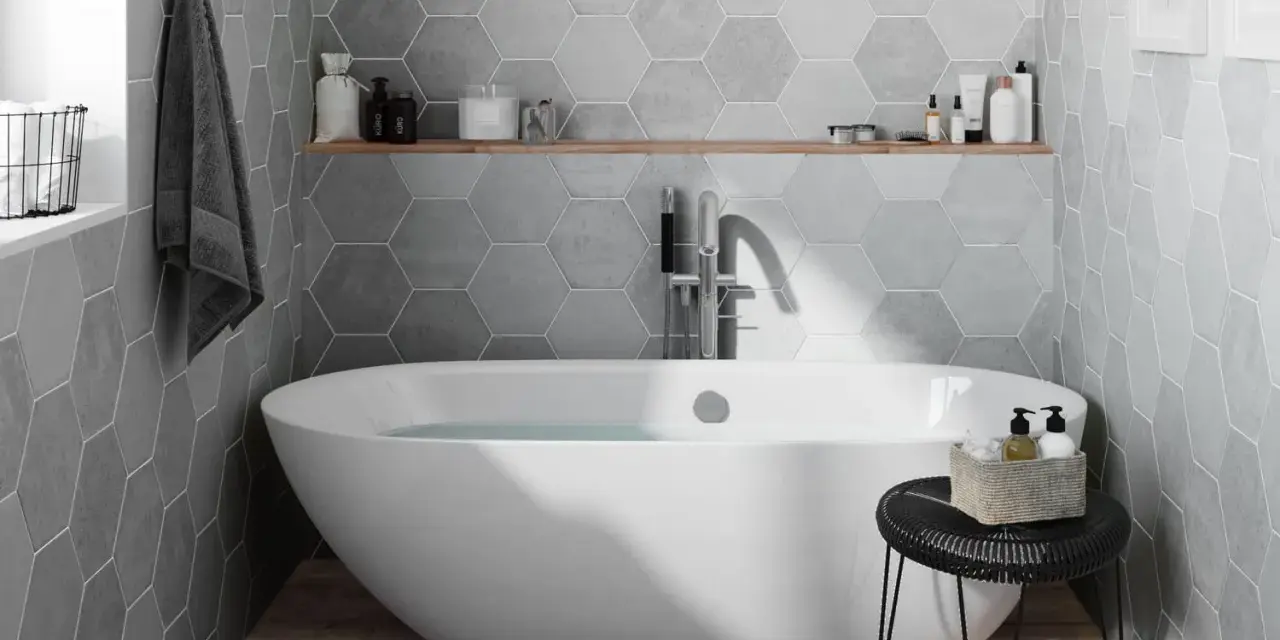Salle de bain moderne avec baignoire îlot, carrelage mural hexagonal gris et étagère en bois.