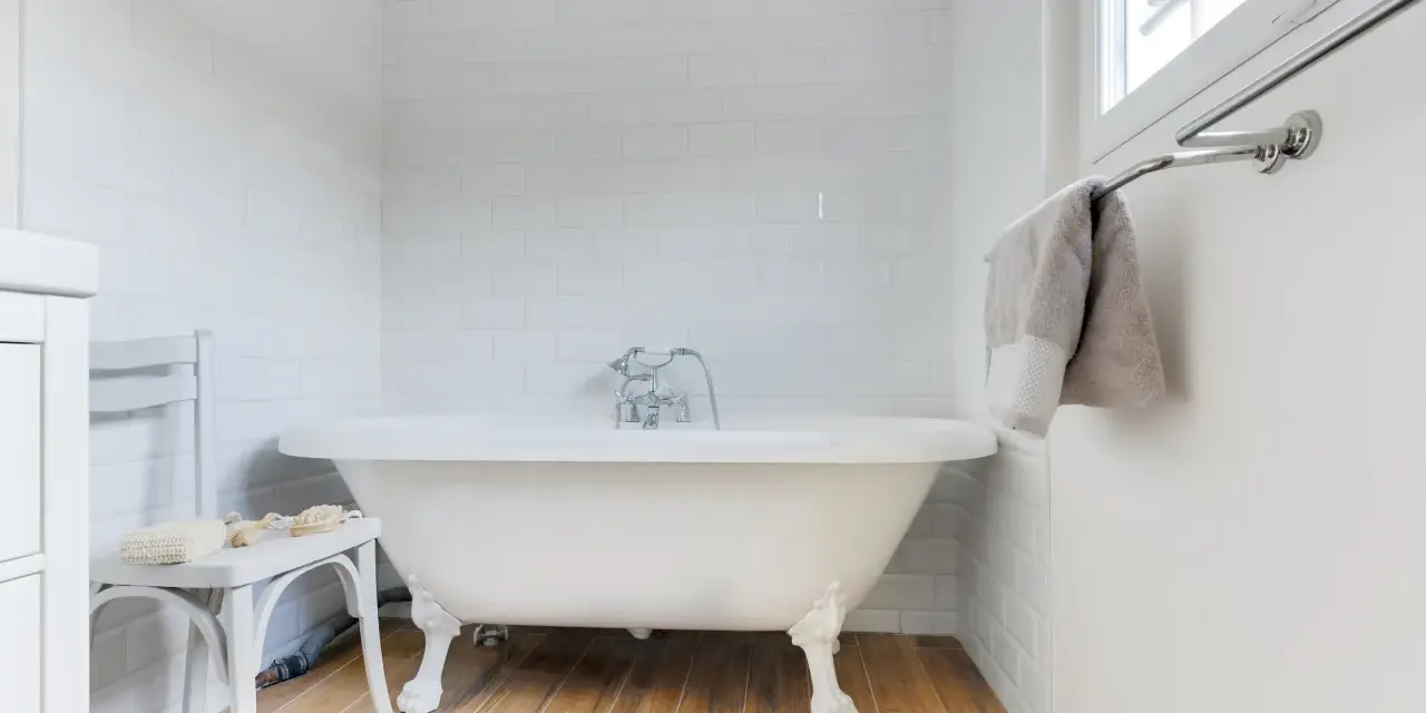Baignoire îlot blanche sur pieds, robinetterie argentée. La hauteur baignoire est standard, avec un petit tabouret à côté.