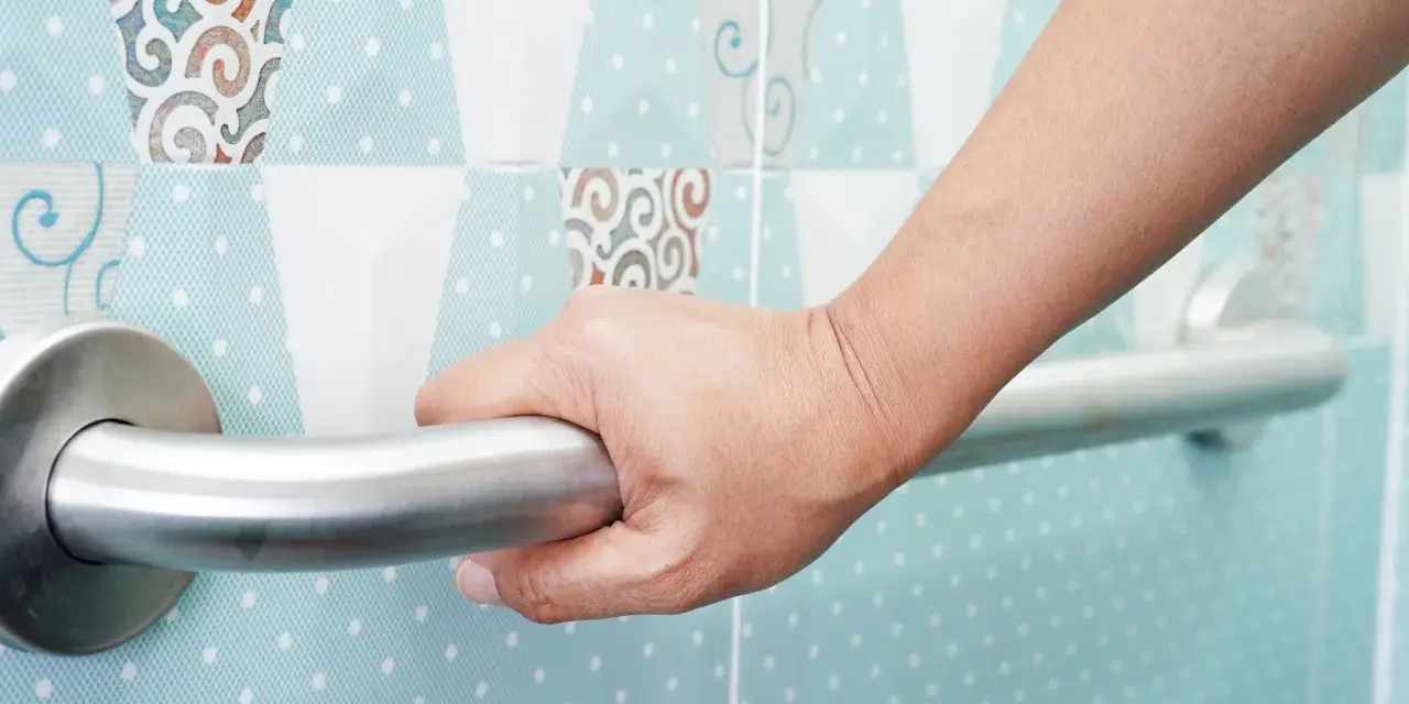 Main d'une personne se tenant à une barre d'appui. La hauteur de la barre de douche PMR est adaptée pour une sécurité optimale.