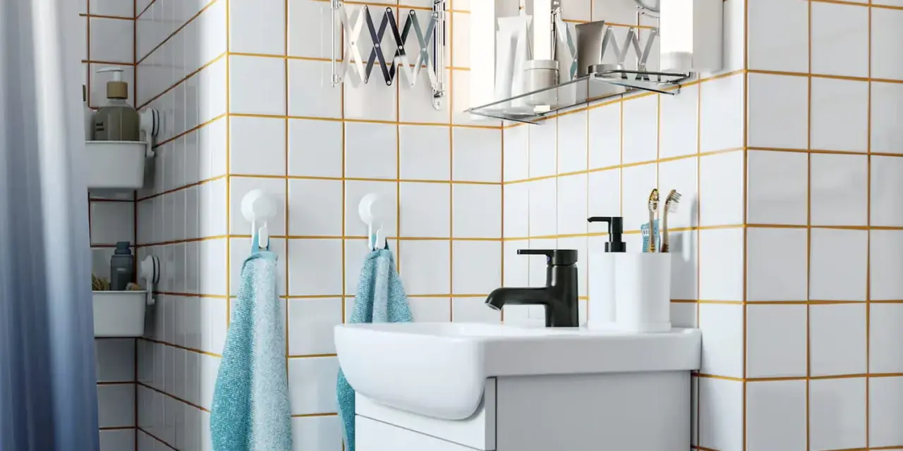 Salle de bain moderne avec carrelage blanc joint gris, lavabo, robinetterie noire et accessoires pratiques.