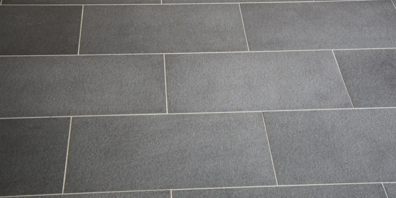 Détail d'un sol en carrelage gris anthracite, avec un joint carrelage couleur crème qui souligne la pose rectiligne.