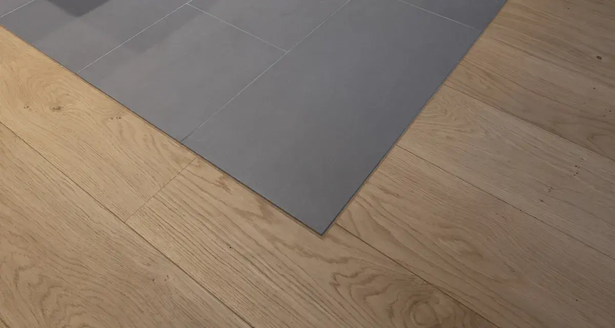 Un coin de sol où le carrelage gris imitation parquet rencontre un parquet en bois naturel. La couleur du joint du carrelage est discrète.