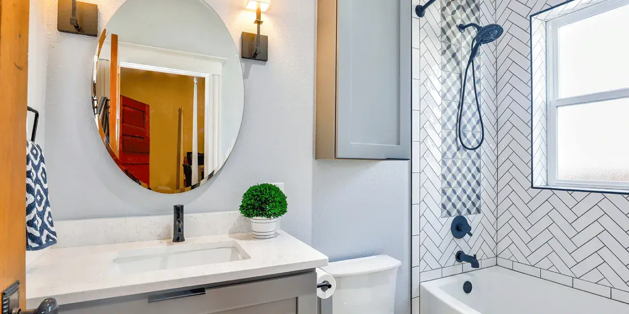 Une petite salle de bain moderne avec baignoire, lavabo gris, miroir rond et carrelage chevrons. Une belle idée pour optimiser l'espace.