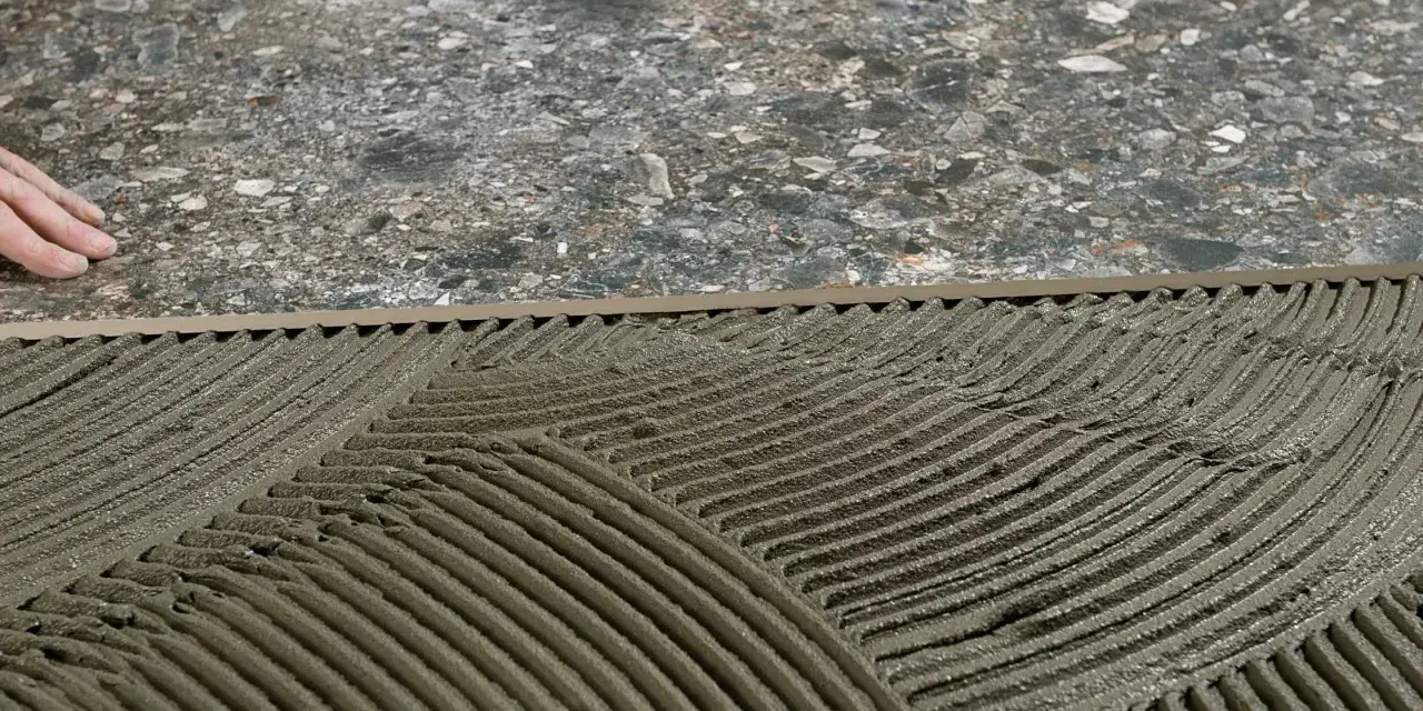 Pose de mortier pour un double encollage de carrelage. Les mains d'un carreleur préparent la surface.