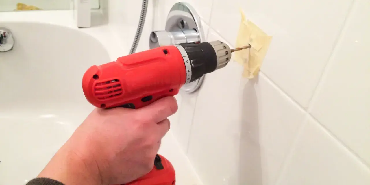Main tenant utilise une perceuse pour percer le carrelage de la salle de bain, afin d'y fixer un accessoire.