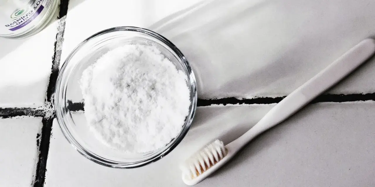 Bicarbonate de soude dans un bol et une brosse à dents sur un carrelage.