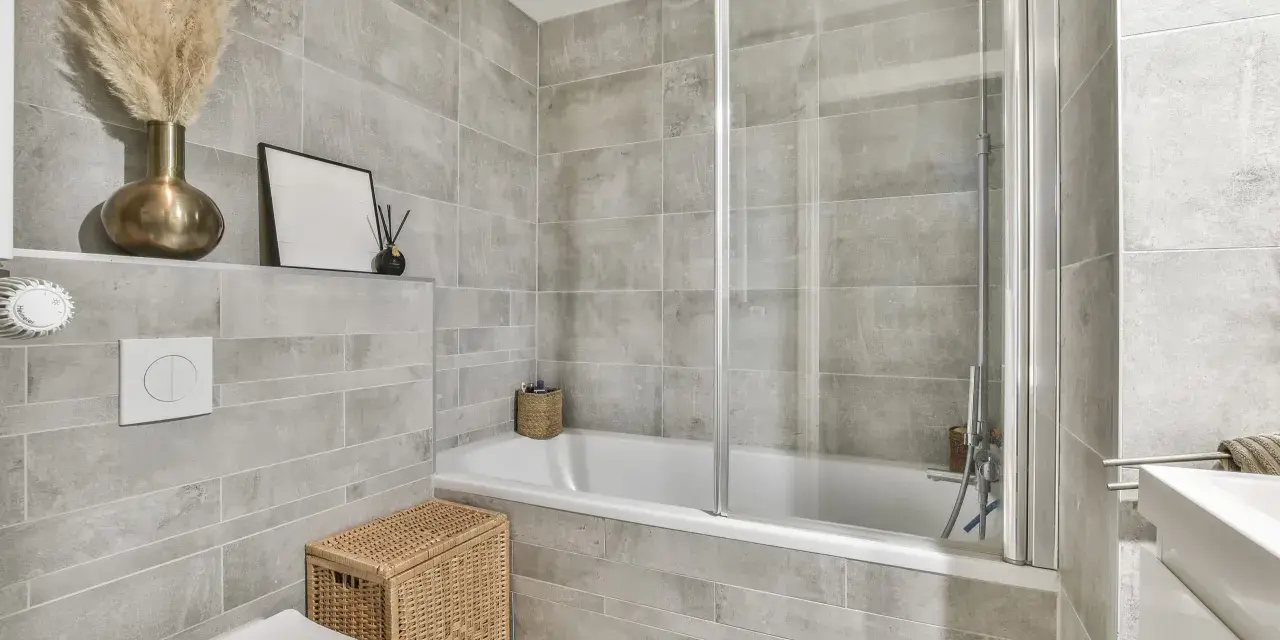 Salle de bain moderne avec carrelage gris. Une baignoire, une douche, un WC et un lavabo. Quelle colle pour carrelage salle de bain ? Une colle adaptée à l'humidité est essentielle.