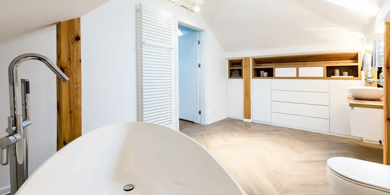 Élégante salle de bain sous pente avec baignoire îlot, lavabo, toilettes et rangements en bois.