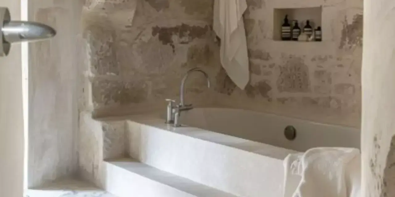 Une **salle de bain méditerranéenne** avec baignoire en pierre brute, robinetterie moderne et serviette blanche suspendue. Ambiance zen.
