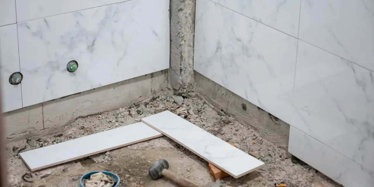 Travaux de pose de faience salle de bain : des carreaux de marbre blanc sont prêts à être installés, avec des outils au sol.