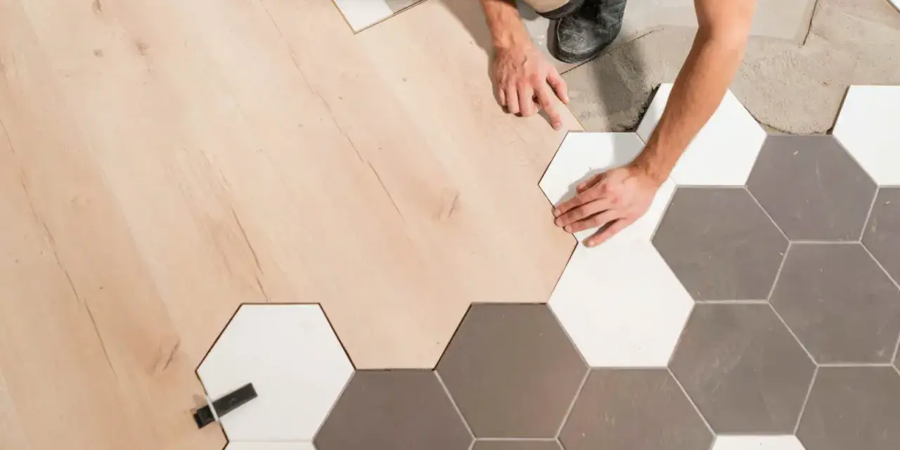Pose d'un parquet bois clair et de carreaux hexagonaux gris et blancs. La jonction parquet carrelage est en cours de réalisation par un artisan.