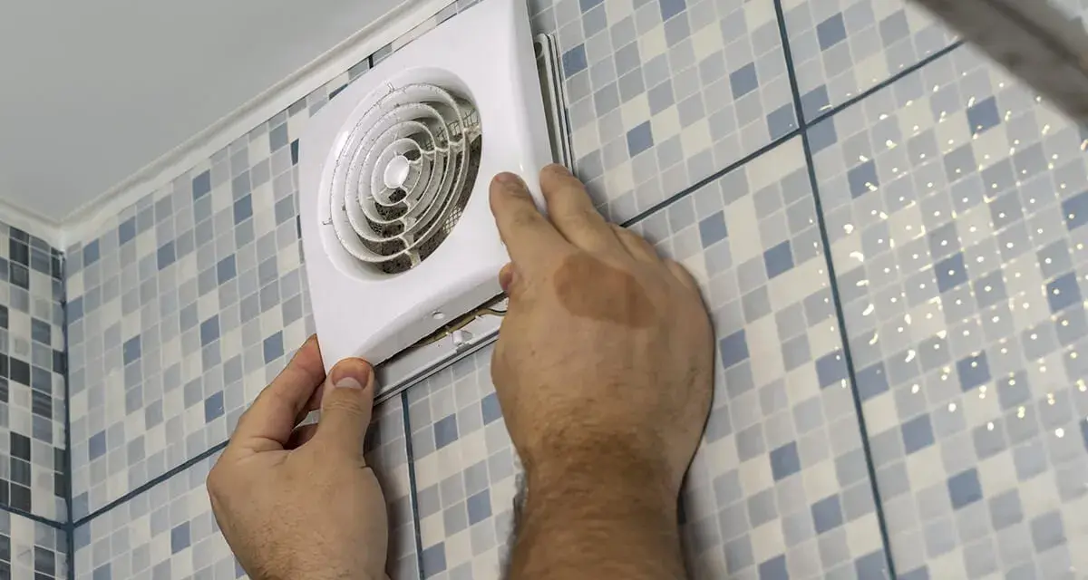 Mains d'un homme installant un ventilateur, une étape clé pour une bonne installation VMC dans une salle de bain carrelée.