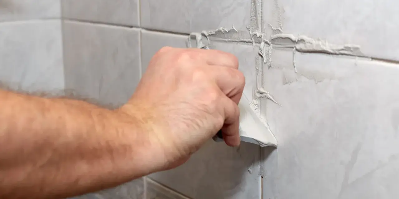Main d'une personne appliquant du mastic sur les joints d'une salle de bain.