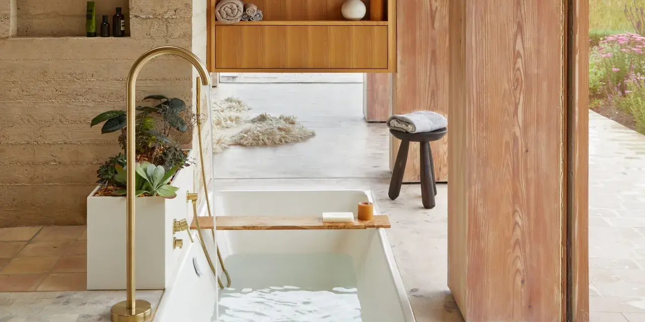 Bain relaxant avec baignoire remplie, robinetterie dorée, plantes et bois. Une belle inspiration salle de bain.