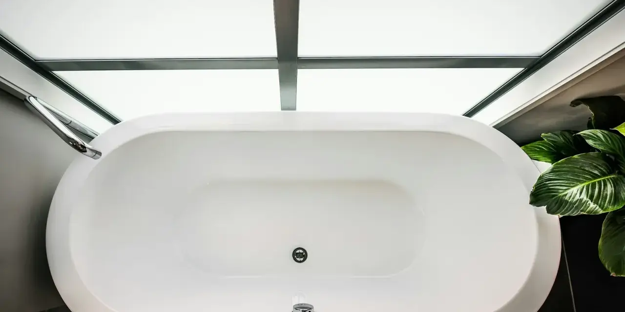 Vue aérienne d'une baignoire blanche moderne, prête à accueillir un bain relaxant. La contenance baignoire est généreuse, sous un puits de lumière.