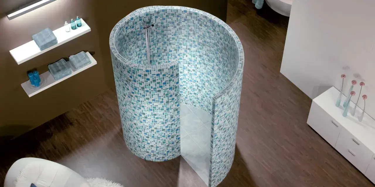 Une douche escargot aux mosaïques bleues et vertes, avec une baignoire et un fauteuil dans une salle de bain moderne.