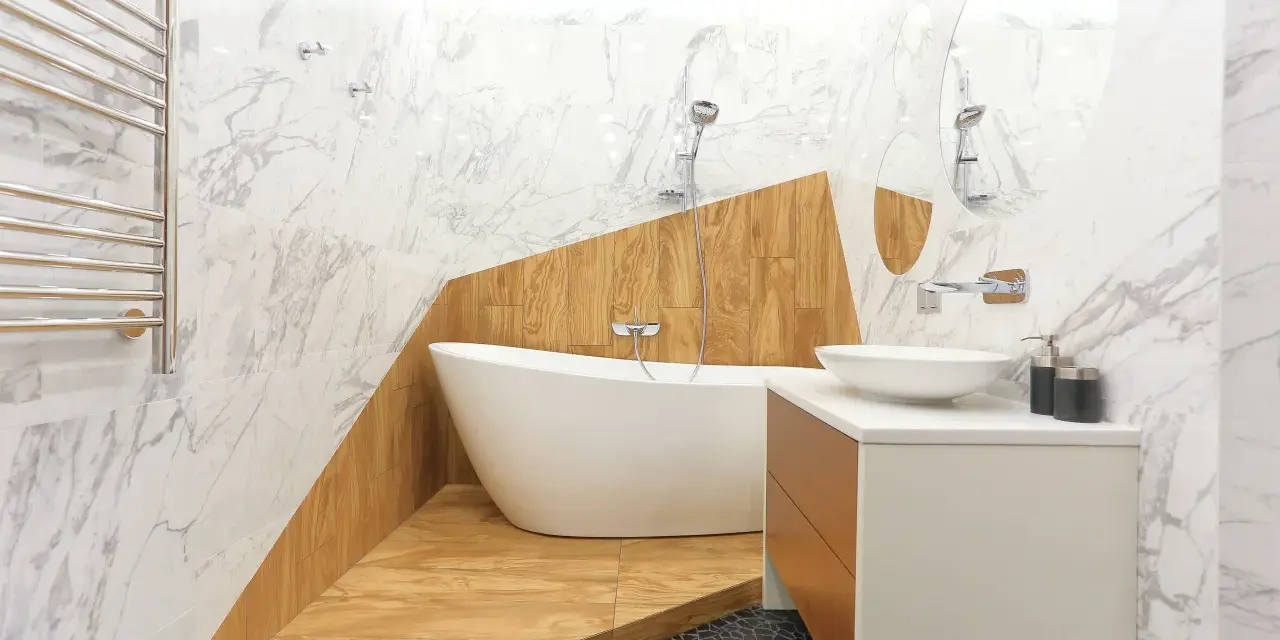 Salle de bain moderne avec baignoire îlot sur une estrade en bois, lavabo, miroir et carrelage marbre.