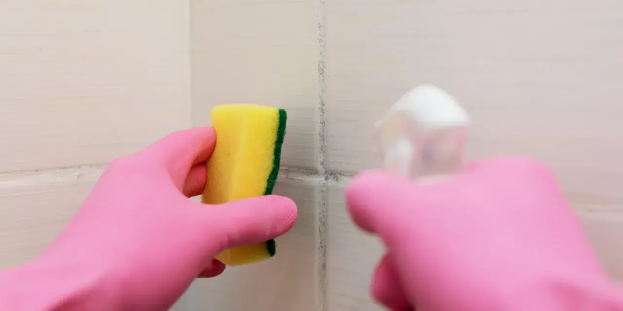 Main rose gantée tient une éponge jaune pour nettoyer une tache sur carrelage qui ne part pas.