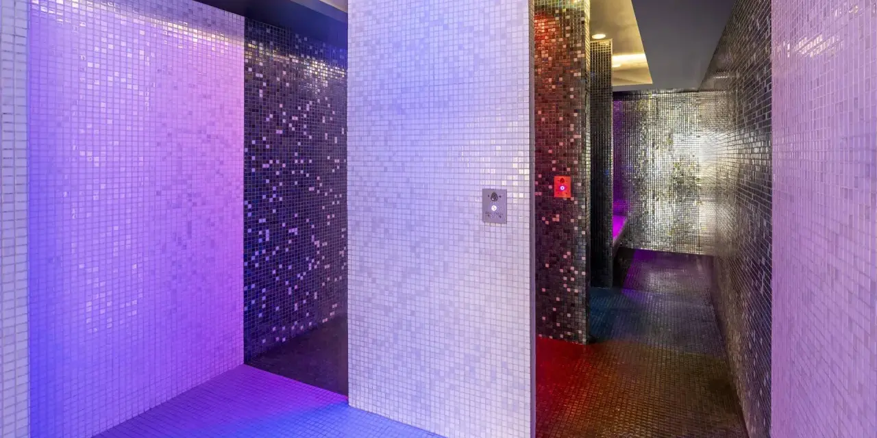 Un espace de détente aux murs recouverts de mosaïques scintillantes, baigné de lumières violettes et bleues. Une invitation à une douche sensorielle immersive.