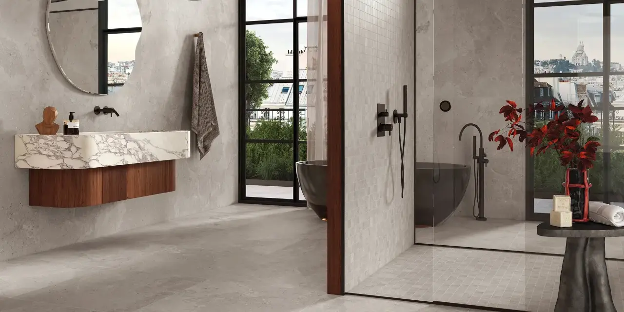 Salle de bain moderne avec baignoire îlot et douche vitrée. Le sol et les murs sont recouverts de carrelage gris, tandis que la paroi de douche est en petite faïence.