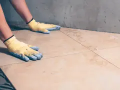 Pose de carrelage : mains gantées ajustant une nouvelle dalle sur la sous couche carrelage.