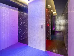 Un espace de détente aux murs recouverts de mosaïques scintillantes, baigné de lumières violettes et bleues. Une invitation à une douche sensorielle immersive.