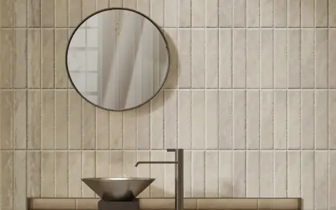 Un lavabo moderne et un miroir rond se reflètent sur un mur de toilette carrelage aux tons sable.