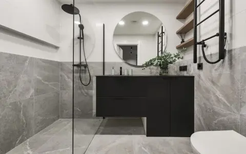 Salle de bain moderne avec douche à l'italienne, meuble suspendu noir, miroir rond et carrelage effet marbre. La construction de cette salle de bain est soignée.