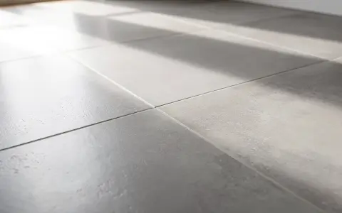 Gros plan sur un carrelage gris moderne, baigné de lumière. On entendrait presque le carrelage qui sonne creux sous les pas.