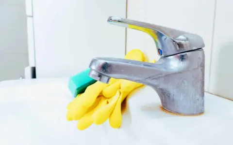 Gants jaunes et éponge verte prêts pour nettoyer robinetterie entartrée.