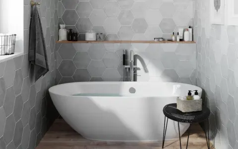 Salle de bain moderne avec baignoire îlot, carrelage mural hexagonal gris et étagère en bois.