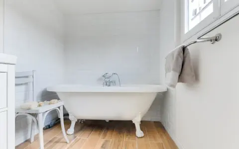 Baignoire îlot blanche sur pieds, robinetterie argentée. La hauteur baignoire est standard, avec un petit tabouret à côté.