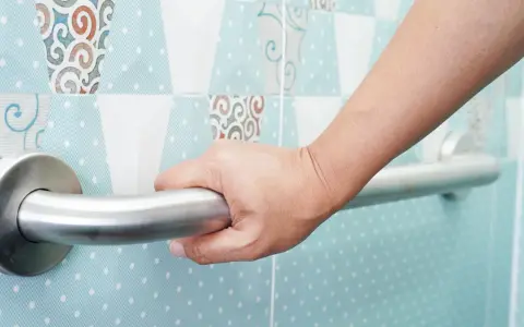 Main d'une personne se tenant à une barre d'appui. La hauteur de la barre de douche PMR est adaptée pour une sécurité optimale.