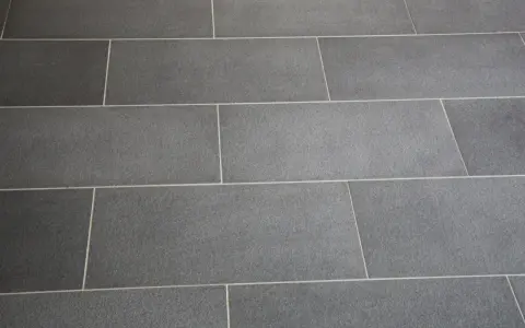 Détail d'un sol en carrelage gris anthracite, avec un joint carrelage couleur crème qui souligne la pose rectiligne.
