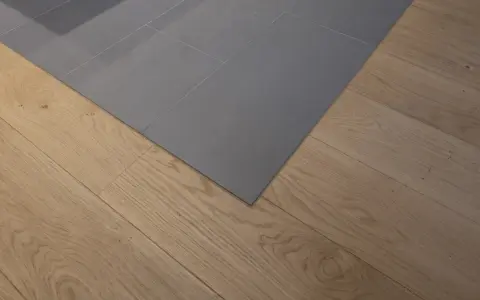 Un coin de sol où le carrelage gris imitation parquet rencontre un parquet en bois naturel. La couleur du joint du carrelage est discrète.