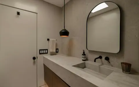 Élégante salle de bain en béton ciré avec un lavabo intégré, un miroir arrondi et un éclairage moderne.