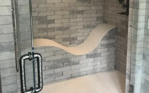 Douche moderne avec un banc ondulé intégré dans le mur de briques. La poignée de la porte en verre est en métal vieilli.