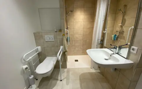 Salle de bain pmr avec douche à l'italienne, WC avec barres d'appui et lavabo. Confort et sécurité pour tous.