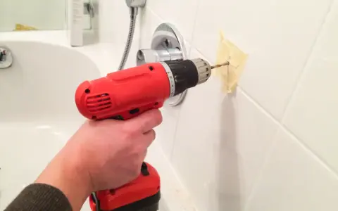 Main tenant utilise une perceuse pour percer le carrelage de la salle de bain, afin d'y fixer un accessoire.