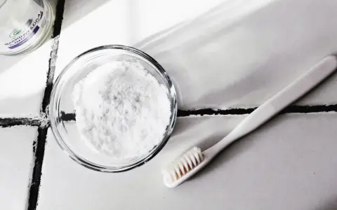 Bicarbonate de soude dans un bol et une brosse à dents sur un carrelage.