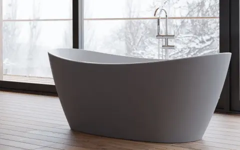 Baignoire îlot moderne, avec robinetterie chromée, devant une grande fenêtre donnant sur un paysage hivernal. Les inconvénients de ce type de baignoire sont son encombrement et la nécessité d'une installation spécifique.