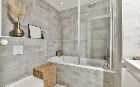 Salle de bain moderne avec carrelage gris. Une baignoire, une douche, un WC et un lavabo. Quelle colle pour carrelage salle de bain ? Une colle adaptée à l'humidité est essentielle.